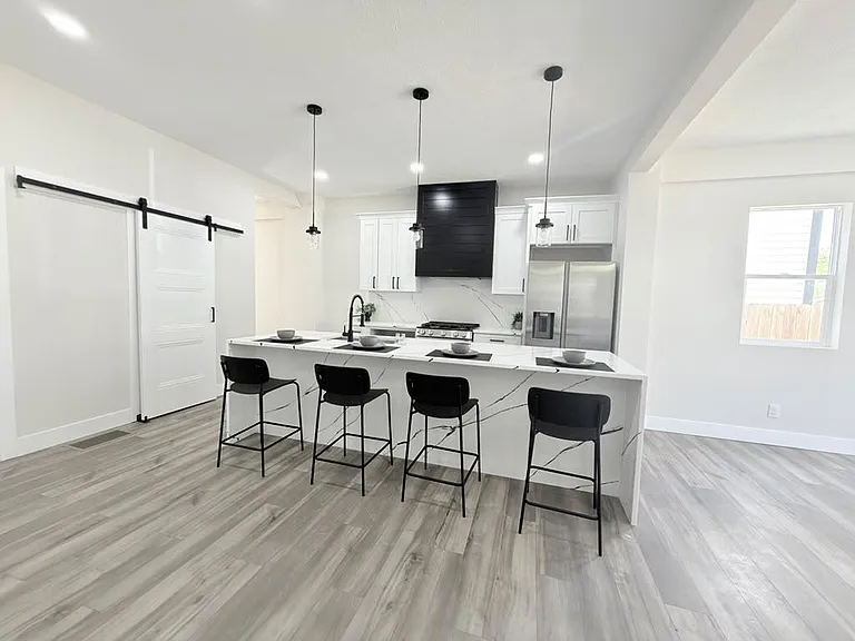 Open kitchen with large waterfall island, bar seating, pendant lighting, and stainless-steel appliances for easy everyday use
