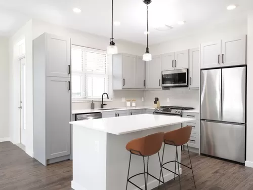 Modern kitchen with stainless steel appliances, white quartz countertop, light grey cabinetry, white tile backsplash, and hard surface flooring - Avalon Amityville