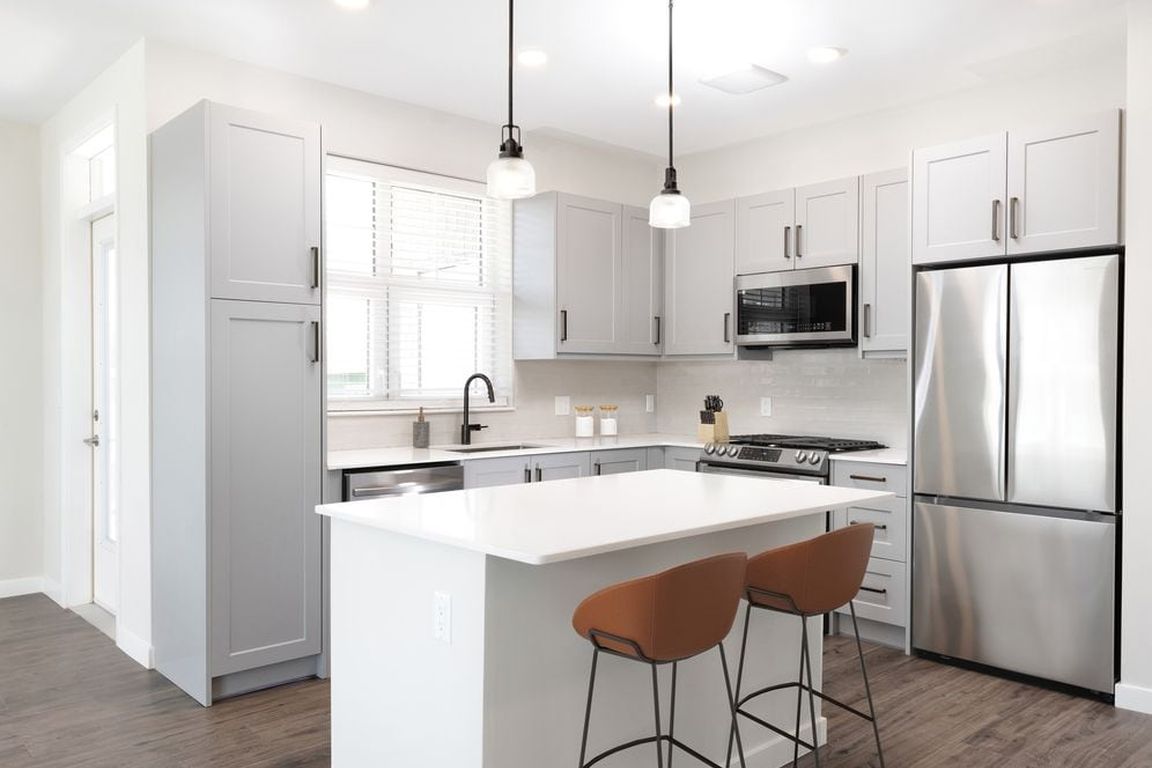 Modern kitchen with stainless steel appliances, white quartz countertop, light grey cabinetry, white tile backsplash, and hard surface flooring