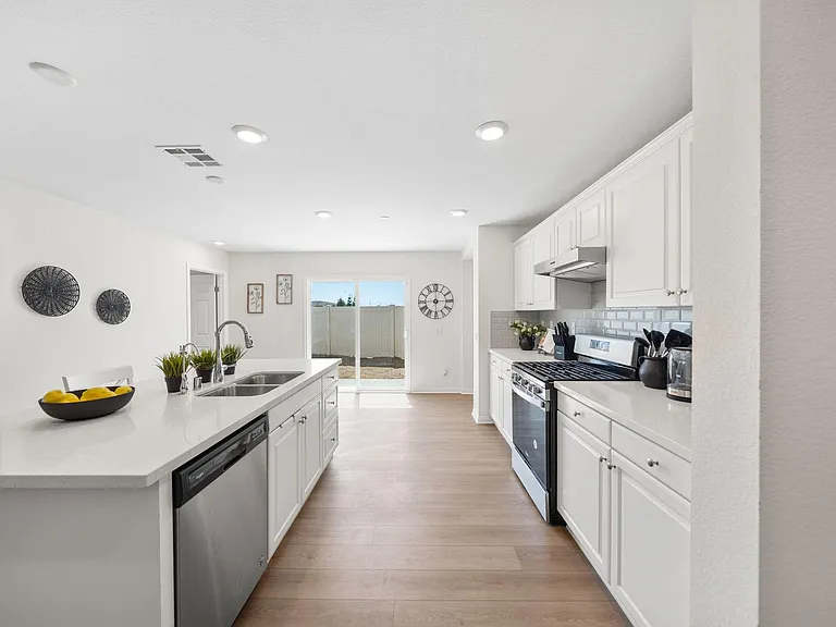 Kitchen with white cabinetry, quartz counters, stainless appliances, and an island sink opening to sliding doors.