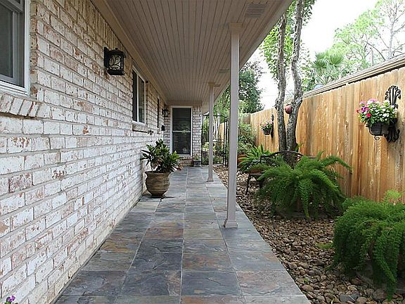Lovely, inviting side patio with beautiful plants and wall hangings leads to front entrance through 