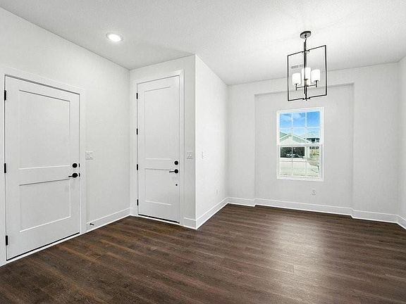 Dark wood-finish flooring, white trim, recessed lighting, and a contemporary chandelier