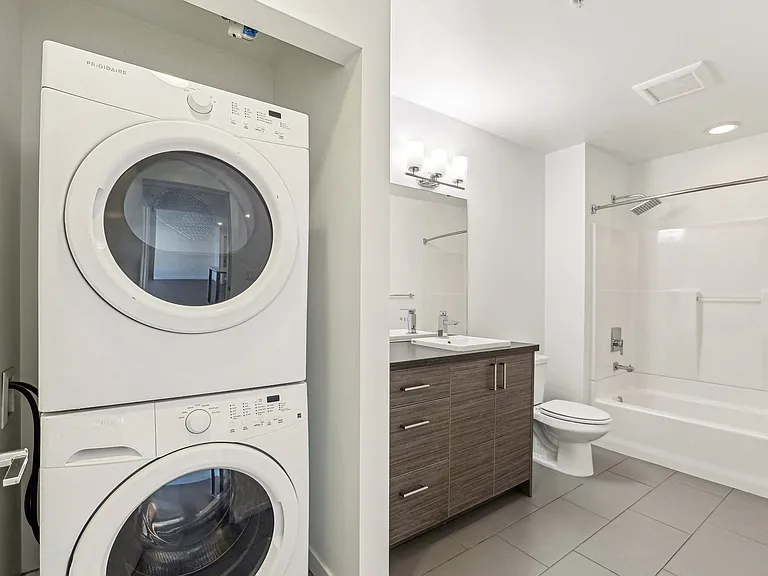 Spacious apartment bathroom at 4400 Alaska in Seattle, WA, featuring a modern vanity, full shower-tub, and convenient in-unit stacked Frigidaire washer and d...
