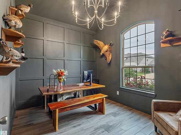 Accent wall with panel molding, arched window with grid pattern, overhead chandelier, and wood-finish flooring