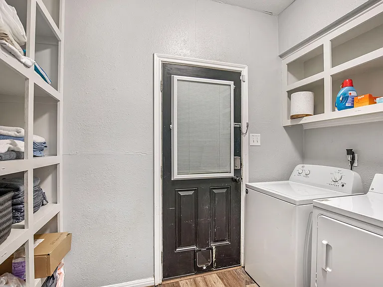 Dedicated laundry room with full-size washer and dryer, open shelving for supplies, and convenient garage access.