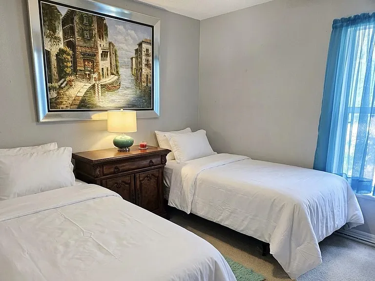 Comfortable bedroom with two twin beds, a nightstand with lamp, and a window with curtains for natural light.