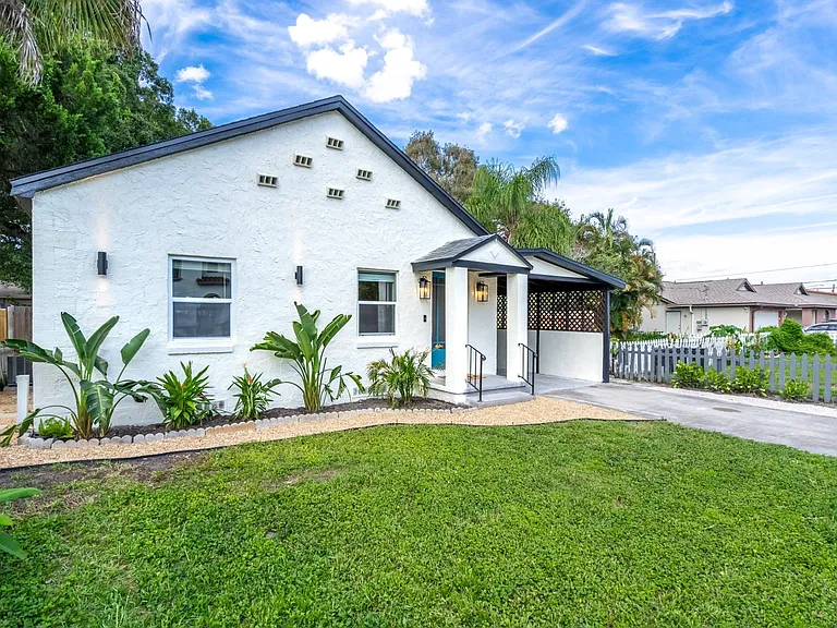 Charming stucco home with covered front porch, landscaped yard, and convenient driveway parking.