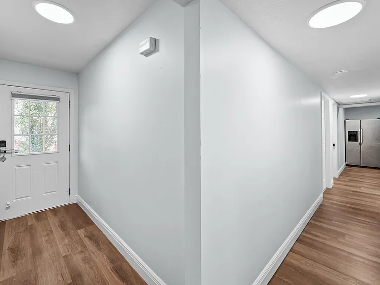 Clean entry hallway with wood-look floors, recessed lighting, and direct access to shared areas and the kitchen.