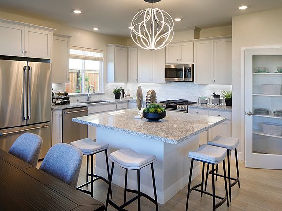 A modern, well-lit kitchen with white cabinets, stainless steel appliances, and a large central isla