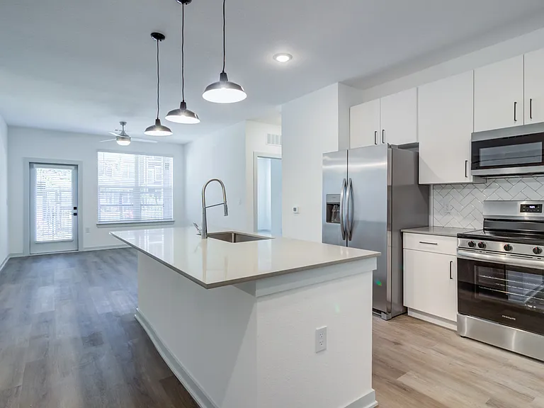 Stainless steel appliances, kitchen island with seating, and white cabinets open seamlessly into the living area, which is flooded with natural light and leading to your own private patio or balcony.