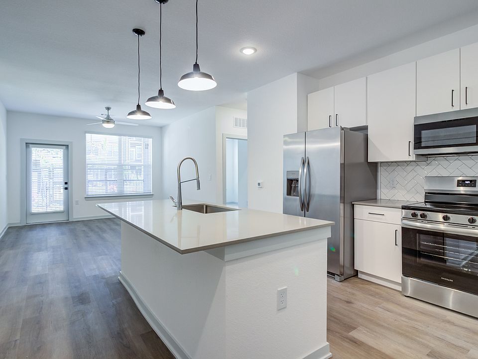 Stainless steel appliances, kitchen island with seating, and white cabinets open seamlessly into the living area, which is flooded with natural light and leading to your own private patio or balcony.