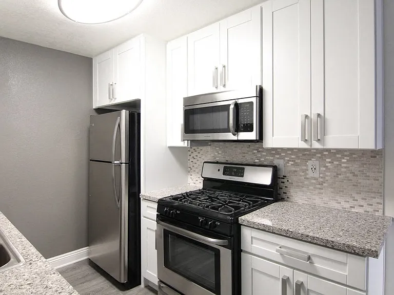 Kitchen with quartz stone counters and stainless steel microwave, oven, fridge, and fixtures.