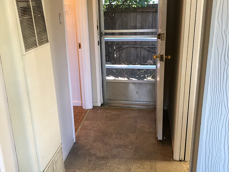 A small hallway leads to the bathroom on the left and the kitchenette on the right. The backdoor is in the middle of the picture