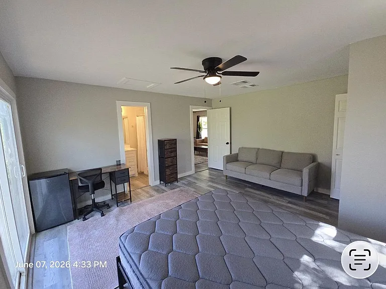 Spacious bedroom setup with a work desk, mini fridge, and seating area, plus convenient access to a nearby bathroom.