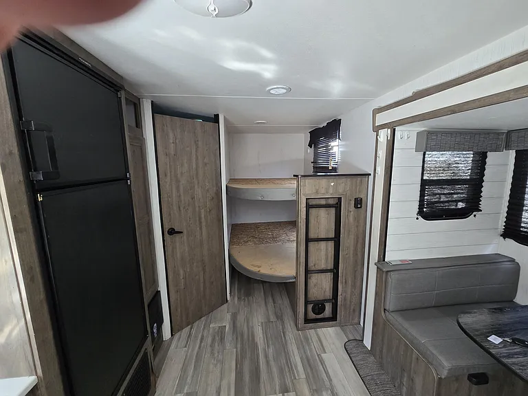 Compact sleeping nook with built-in bunk beds, ladder access, and a small seating bench beside a window.