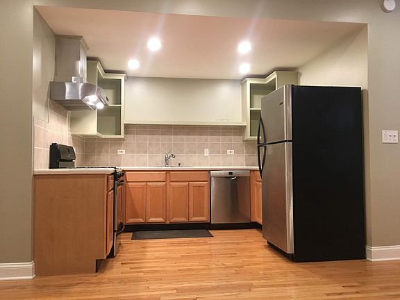 Bright kitchen with open shelving and stainless appliances including gas range, refrigerator, microwave (next to fridge), and a Bosch dishwasher.