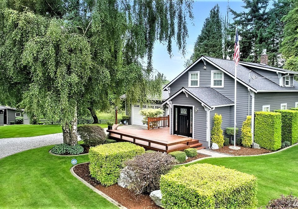 Stunning entrance showing off sculpted bushes, large deck leading up to striking front door of undated Chraftsman home. 600 ft garage added on to the left and far left is an additional outbuilding tastefully done! 50 yr roof only 2 yrs old!!