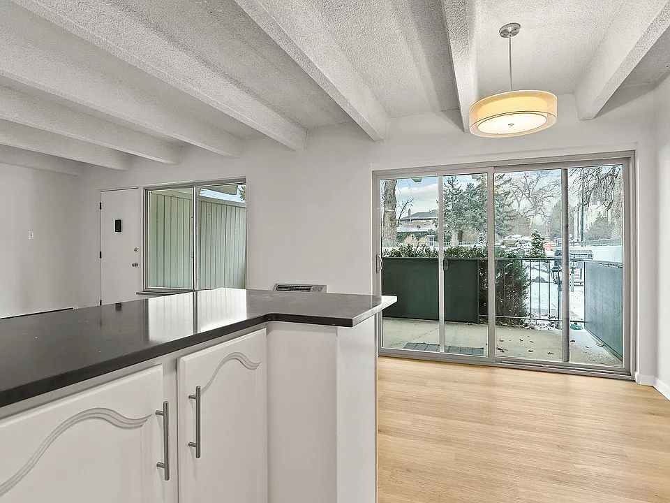 Modern apartment interior showcasing a sleek kitchen countertop leading to a bright dining area with large sliding glass doors opening to a cozy balcony view.