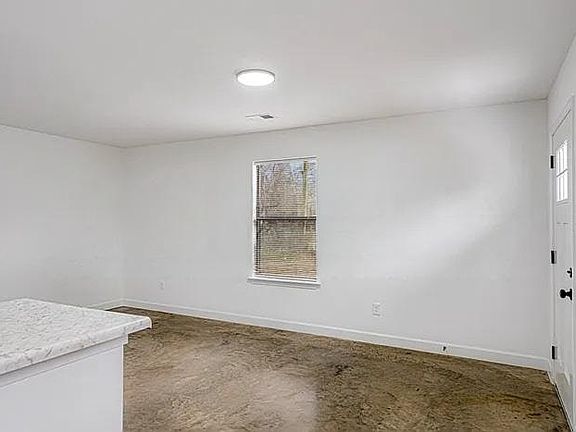 A sun-drenched, minimalist room featuring crisp white walls and industrial-style polished concrete floors.