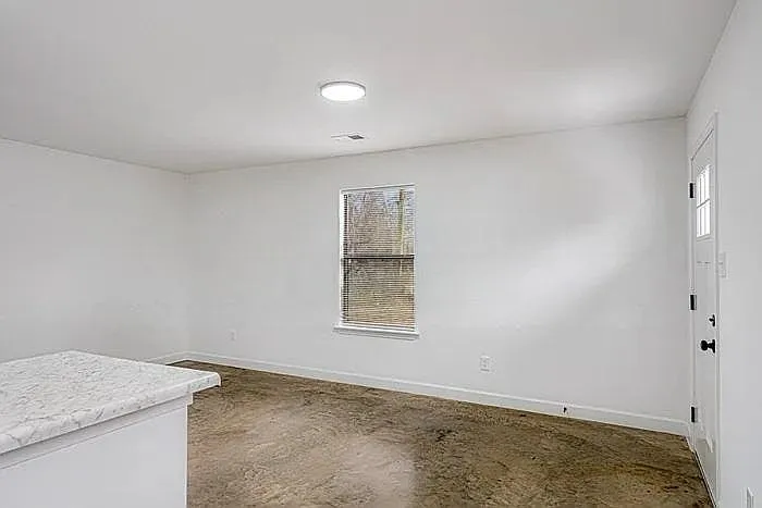 A sun-drenched, minimalist room featuring crisp white walls and industrial-style polished concrete floors.