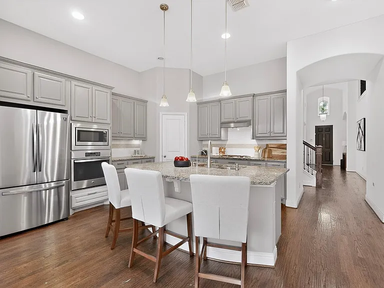 A modern kitchen featuring a kitchen island, stainless steel appliances, warm hardwood floor and decorative lighting, creating a stylish and inviting atmosphere.