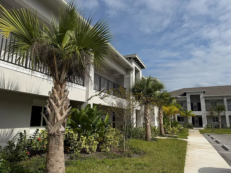 Inviting apartment complex with lush landscaping and palm trees, offering a serene and tropical ambiance.