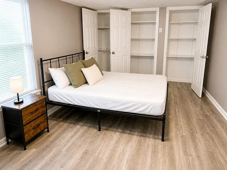 Spacious bedroom with a large window, wood-look flooring, and two open closets with shelving for easy storage.