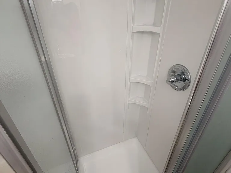 Enclosed shower stall with sliding glass doors, molded wall surround, and built-in corner shelving for toiletries.