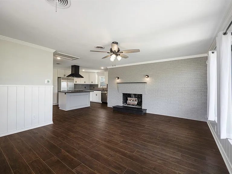 Unfurnished family room featuring ceiling fan, a fireplace, dark hardwood / wood-style flooring, brick wall, and ornamental molding