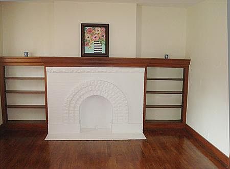 View of living room with original hardwood floors, mock fireplace and side bookshelves. Window air conditioning unit in this roo