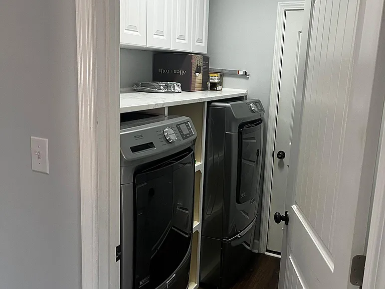 Dedicated laundry room with included front-loading washer and dryer on drawer risers, cabinetry, and additional storage.