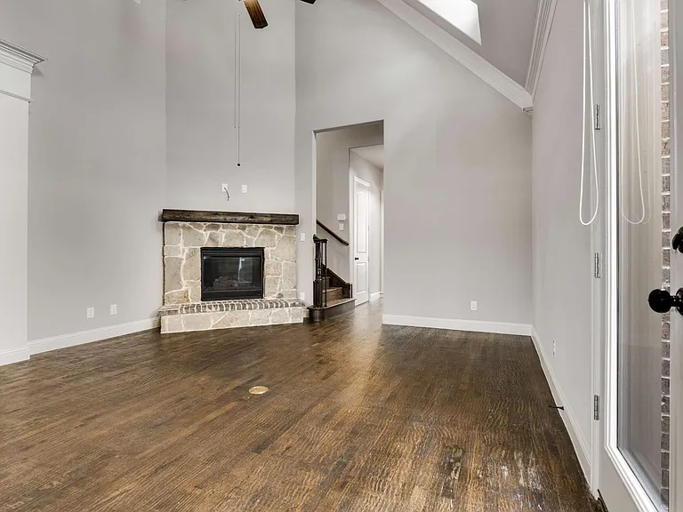 Living room featuring a skylight, high vaulted ceiling, ceiling fan, a stone fireplace, and wood floors