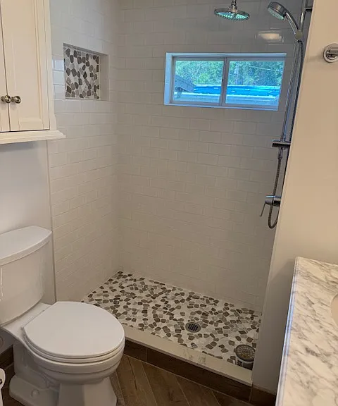Spacious shower with floor to ceiling decorative tile with chrome shower and wand.