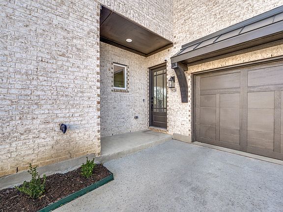 White brick exterior with dark trim accents, featuring a paneled garage door and a covered entryway with a full-light door