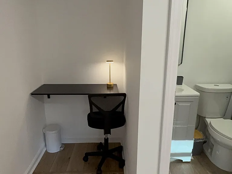 Dedicated work nook with a wall-mounted desk and task lighting, set just outside a nearby bathroom for convenience.