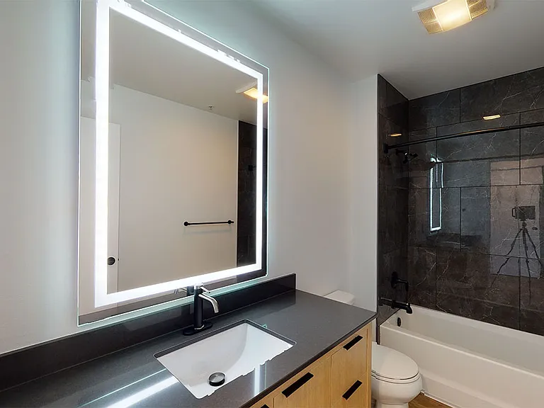 Apartment bathroom with wood-style flooring and LED vanity mirror.