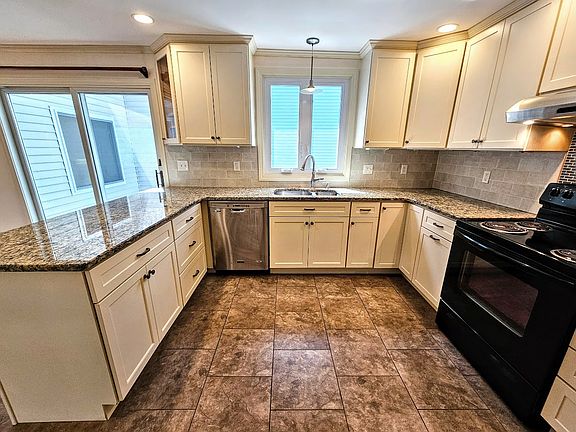 kitchen with dishwasher, electric stove, double sink with garbage disposal, granate counter tops, cabinets, tile splash guard