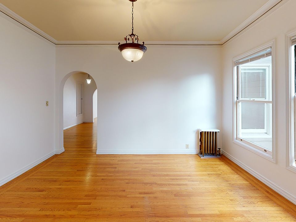 Room with hardwood floor, ceiling light, windows, archway, and radiator
