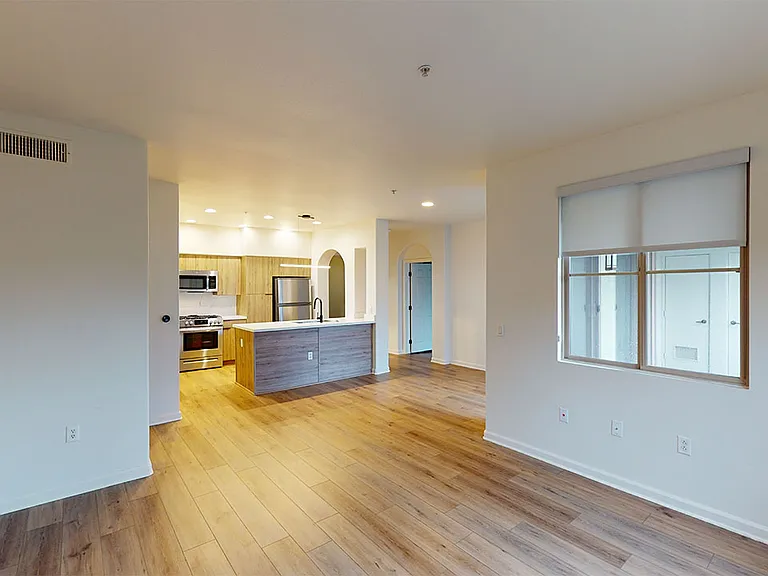 Apartment kitchen with stainless steel appliances, dining and living room with wood-style flooring.