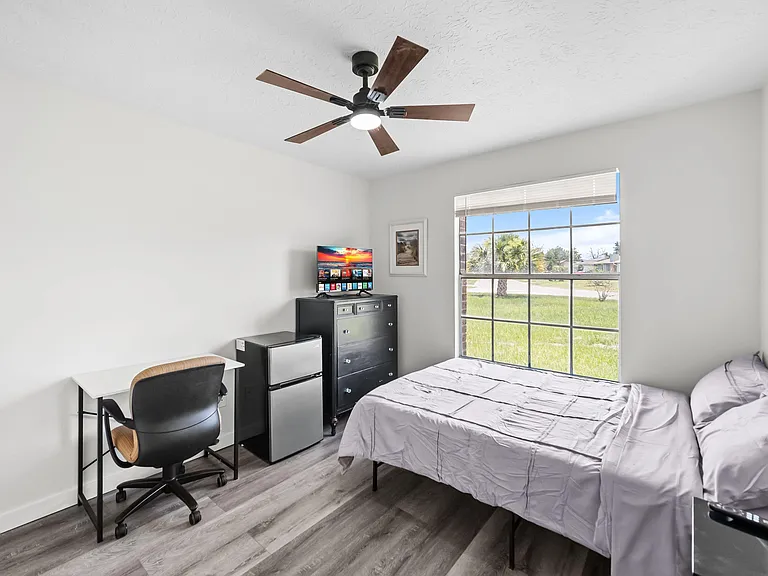 Private bedroom with a large window, ceiling fan, and vinyl plank flooring, plus a desk, dresser, and mini-fridge.