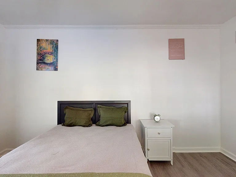 Simple bedroom with double bed, nightstand, and neutral walls offering flexible layout space for personal storage.