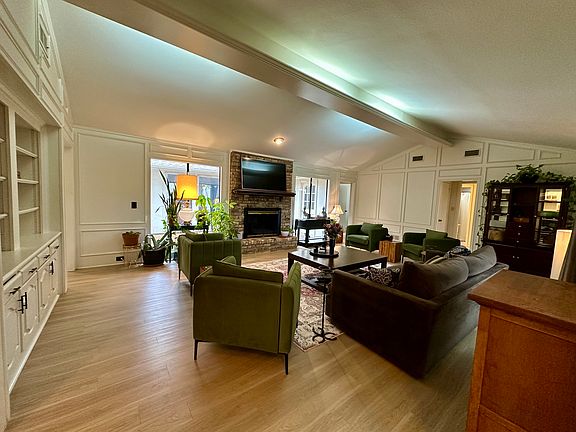 Living area featuring a fireplace, a decorative wall, vaulted ceiling with beams, light wood-type flooring.