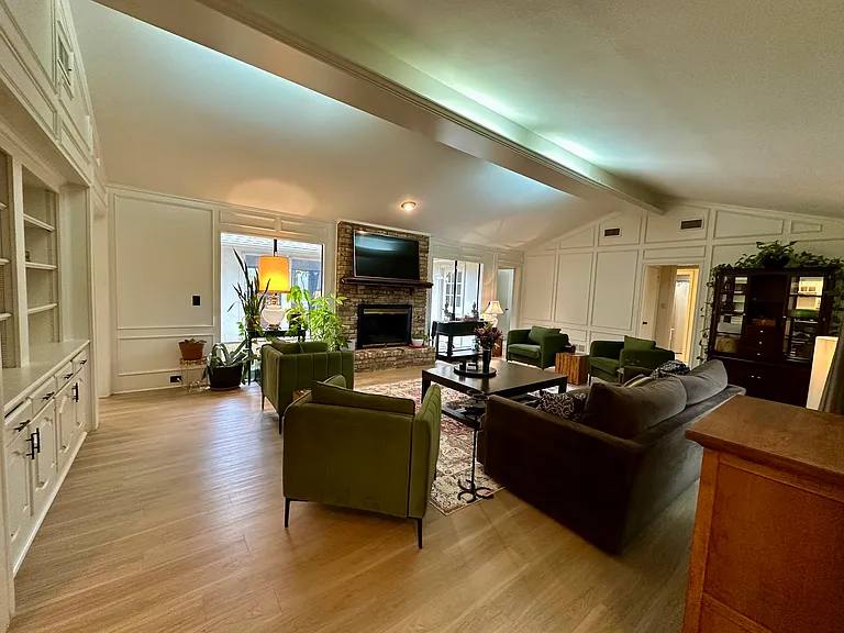 Living area featuring a fireplace, a decorative wall, vaulted ceiling with beams, light wood-type flooring.