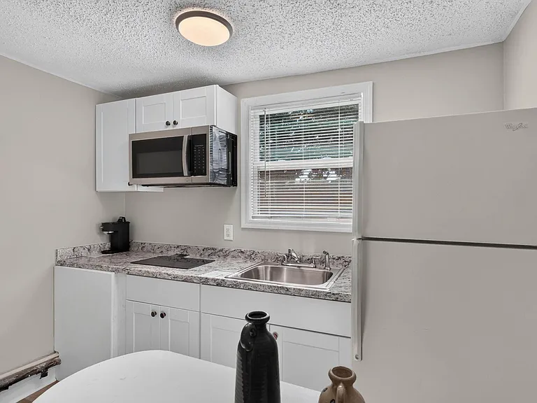 Efficient kitchen with ample cabinet storage, laminate counters, stainless sink, and included microwave and refrigerator.