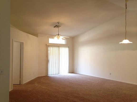 Large, combined lining room and dining room with cathedral ceilings, ceiling fan, and pot shelves. Fresh paint and new carpet. Sliding glass doors open onto a covered patio.