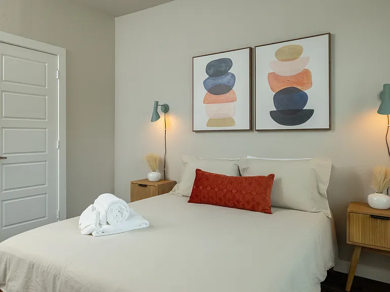 Cozy third bedroom with a queen bed, unique green hanging light fixtures on each side, and plenty of natural light_fresh, stylish, and serene. This bedroom is located upstairs.