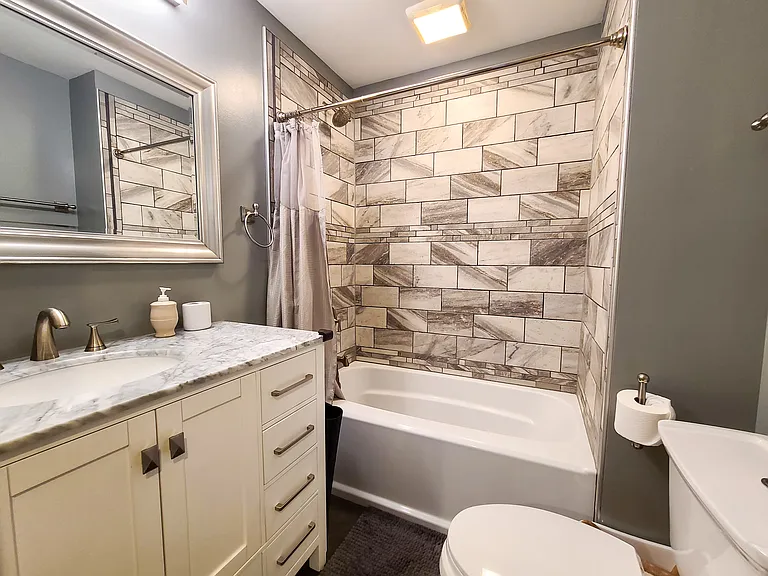 Hallway bathroom with tiled shower and full bathtub. Granite countertop on vanity.