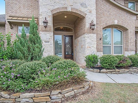 Stone and brick porch entry with lush landscaping and wrought iron and glass front door.