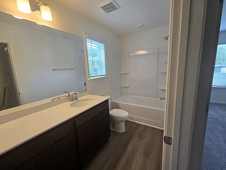 Shared full bath showing bath tub, window, large size mirror covering both the sinks and commode