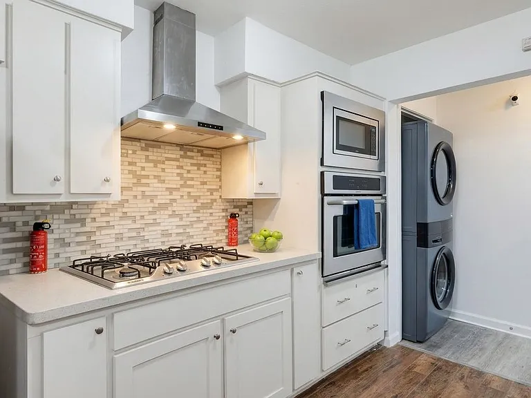 Well-appointed kitchen with gas cooktop, vent hood, tile backsplash, ample cabinetry, and in-unit stacked washer/dryer.